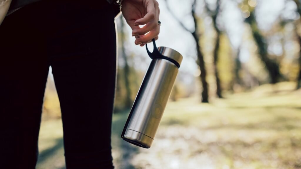Persoon houdt een RVS drinkfles met draaglus vast tijdens een wandeling buiten in het bos